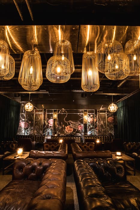Dimly lit lounge featuring tufted leather sofas and warm, glowing birdcage-style pendant lights.